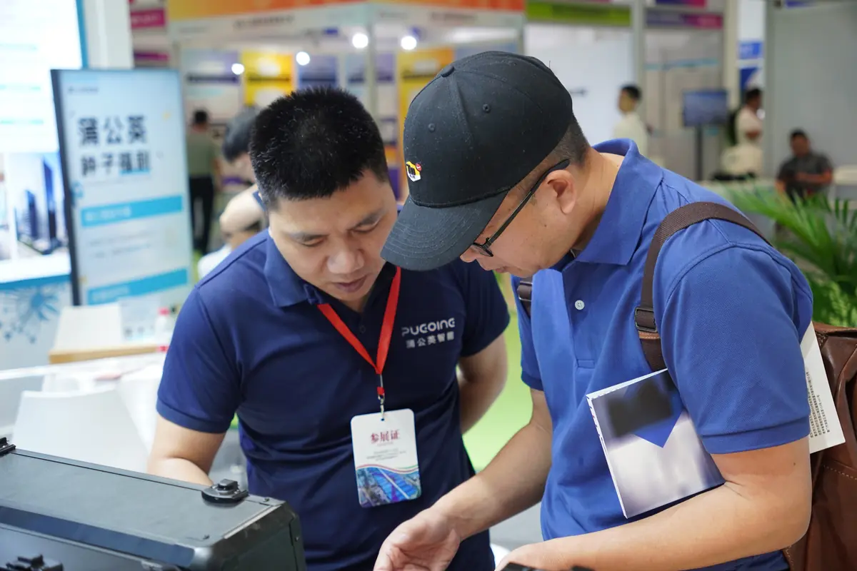 A PUGOING staff member and a visitor examine demonstration equipment at the booth